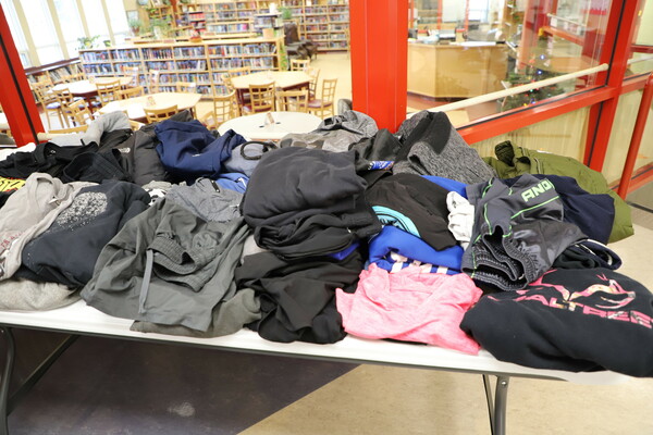 A table full of folded clothing from the lost and found sits in front of a window into the library.